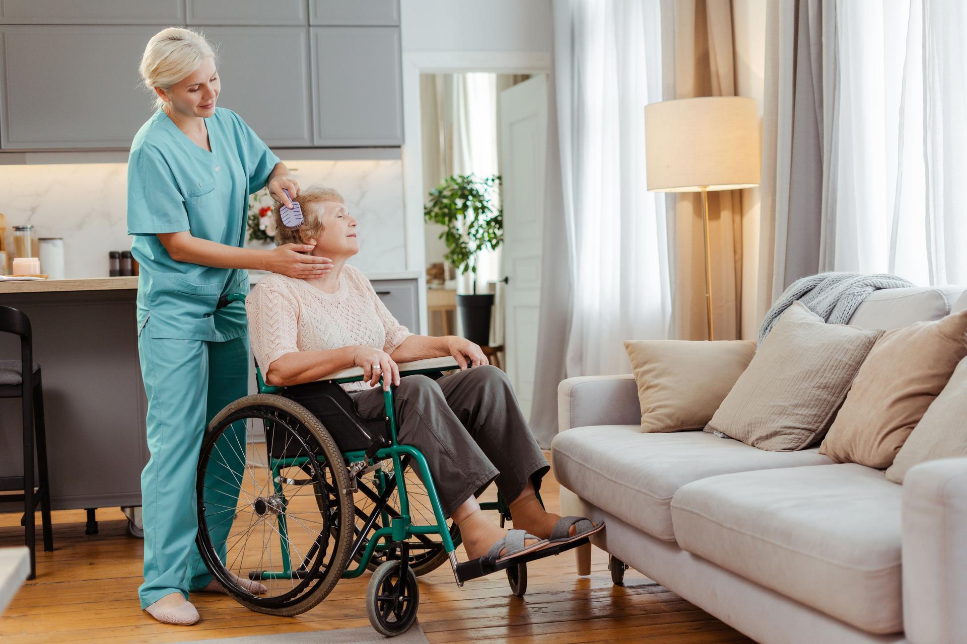 Nurse brushing elderly woman’s hair while offering support, caring for senior in wheelchair at home in Port Charlotte, FL.